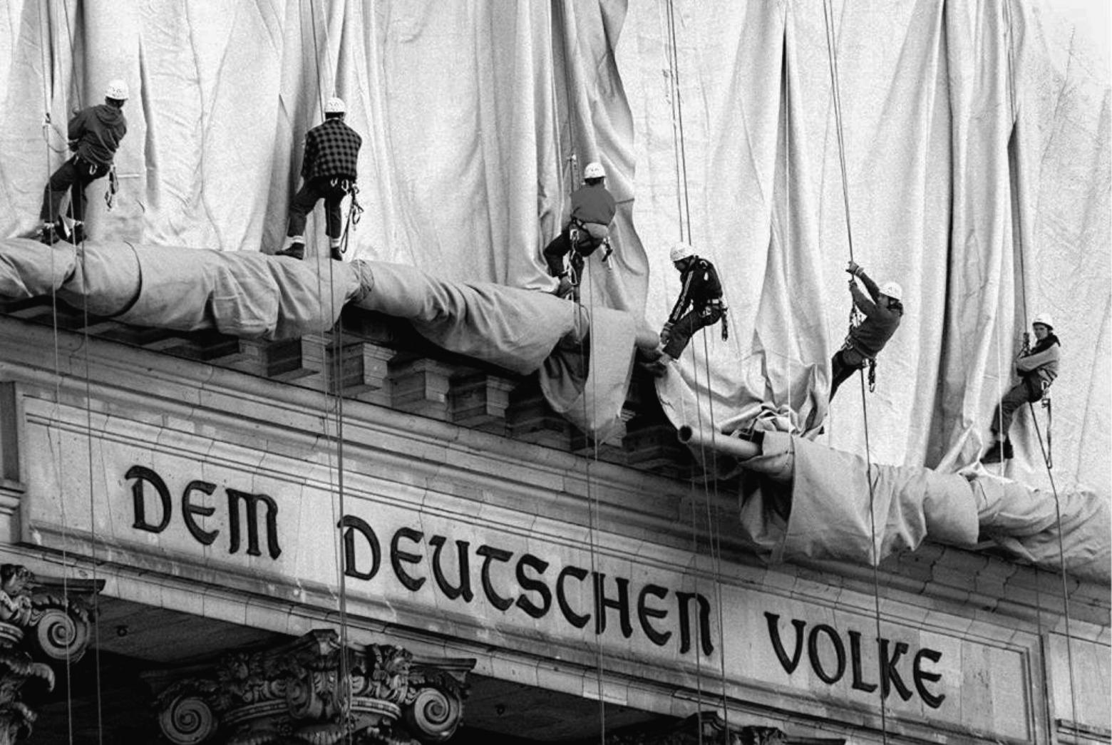 23. Juni 1995, Berlin: Gewerbekletterer rollen die Verhüllungsplanen für den Berliner Reichstag vom Giebel des Bauwerks ab