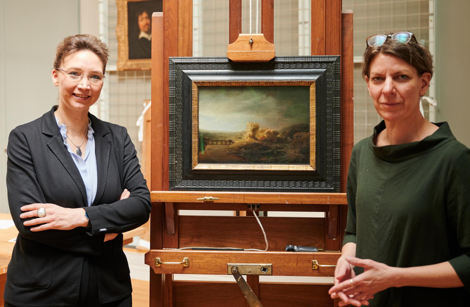 Dagmar Hirschfelder (l), Direktorin der Gemäldegalerie, und Katja Kleinert, Kuratorin der Gemäldegalerie, neben dem Gemälde "Landschaft mit Bogenbrücke" in der Restaurierungswerkstatt der Gemäldegalerie