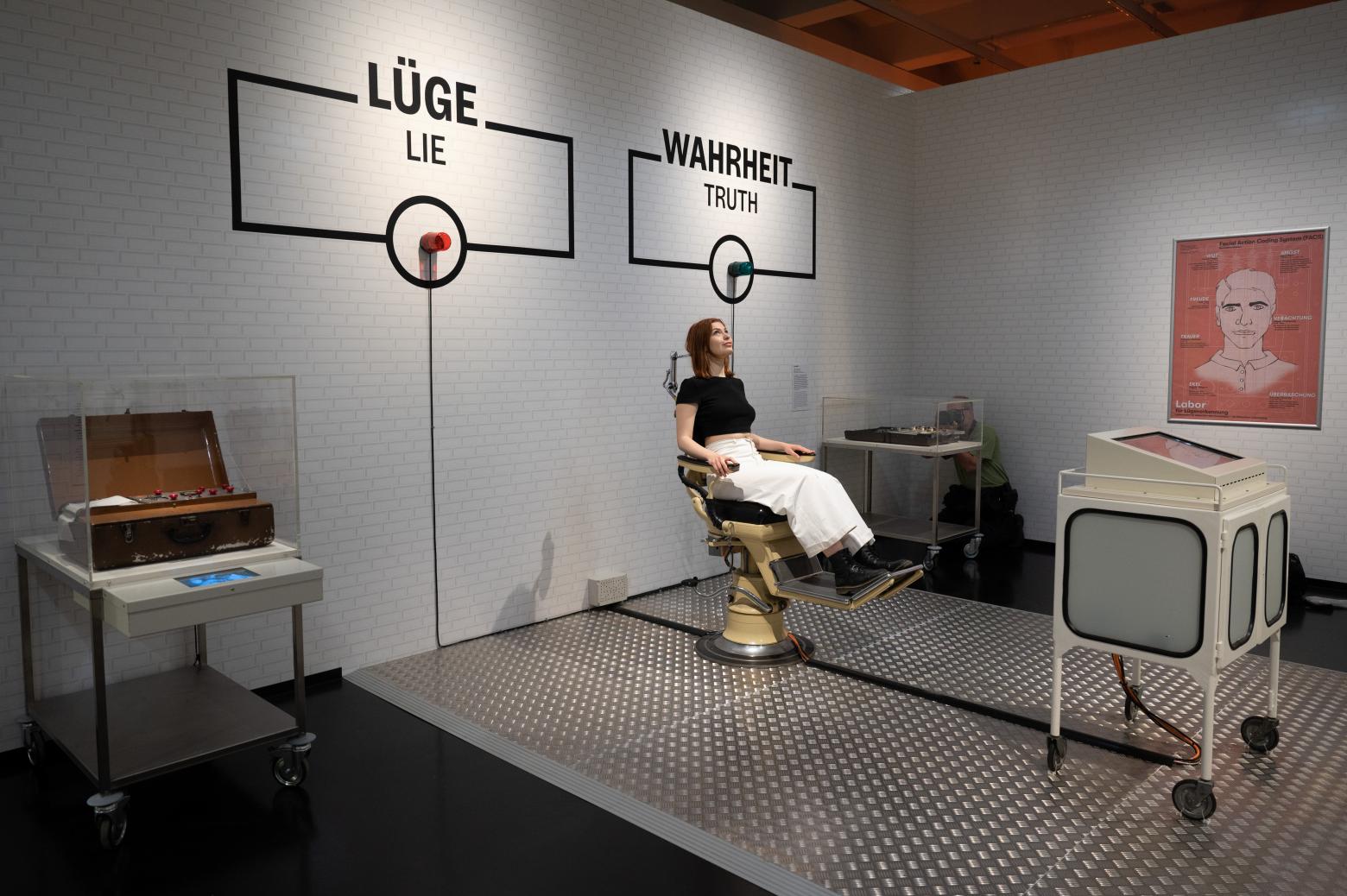 Eine Mitarbeiterin des Deutschen Hygiene-Museums Dresden sitzt in der Ausstellung "Fake. Die ganze Wahrheit" zwischen zwei Lügendetektoren