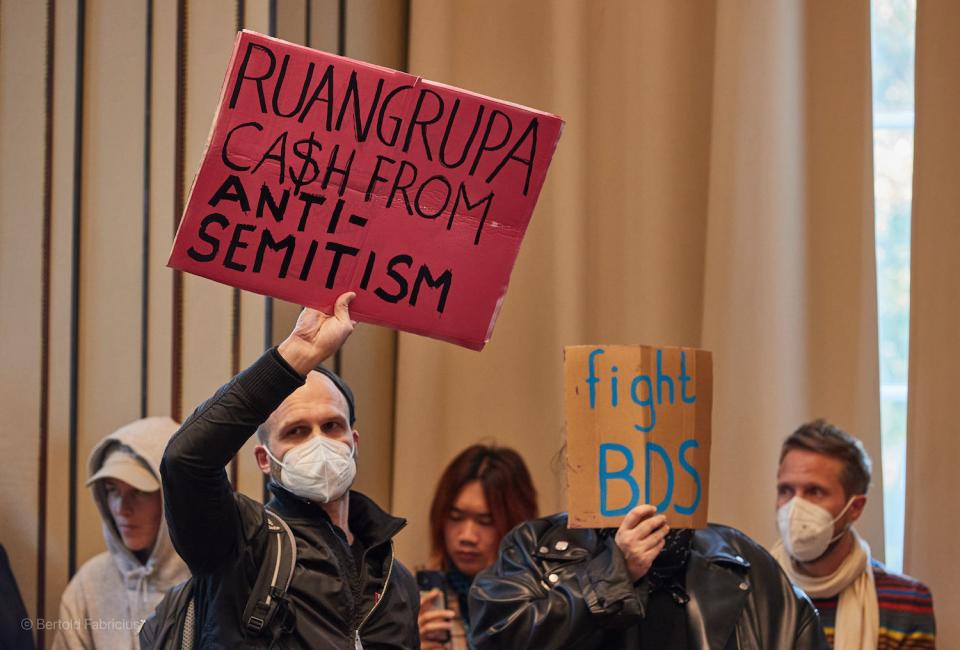 Protestierende halten in der Aula der Hochschule für bildende Künste Hamburg (HfbK) Tranparente mit der Aufschrift "Ruangrupa C$sh From Antisemitism" und "Fight BDS" während einer Rede hoch