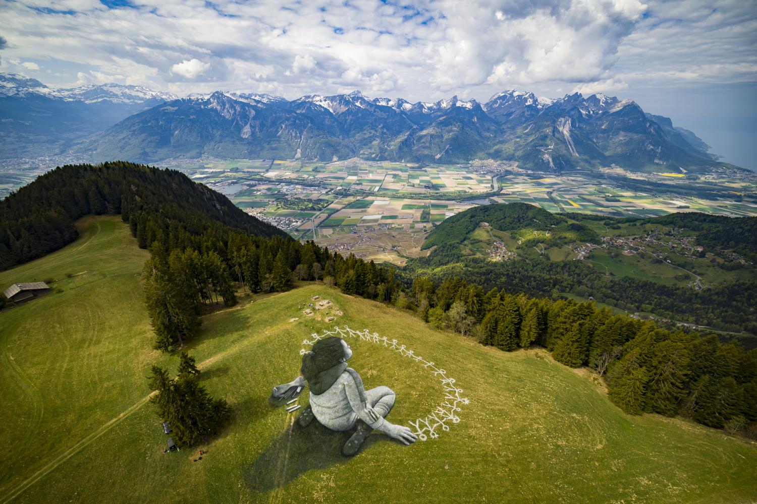 Riesiges Land-Art-Gemälde des schweizerisch-französischen Künstlers Saype mit dem Titel "Jenseits der Krise" über eine Wiese des alpinen Ferienorts Leysin