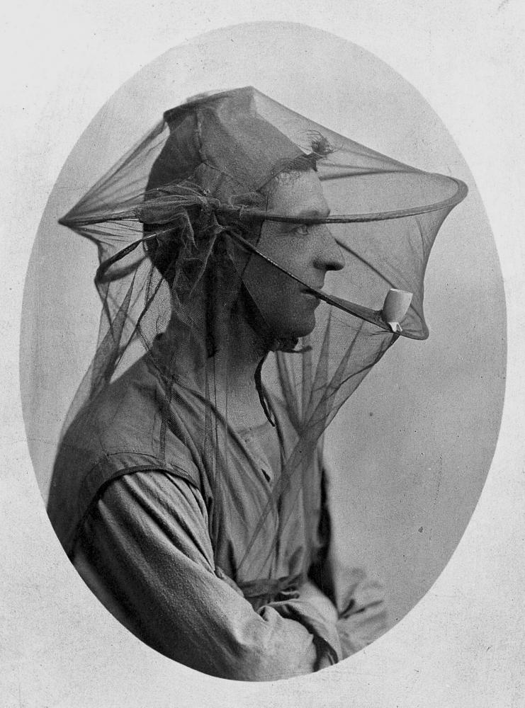 Unbekannter Künstler "Mosquito headnet with a cap, modelled by a man in profile smoking a pipe", 1902/18
