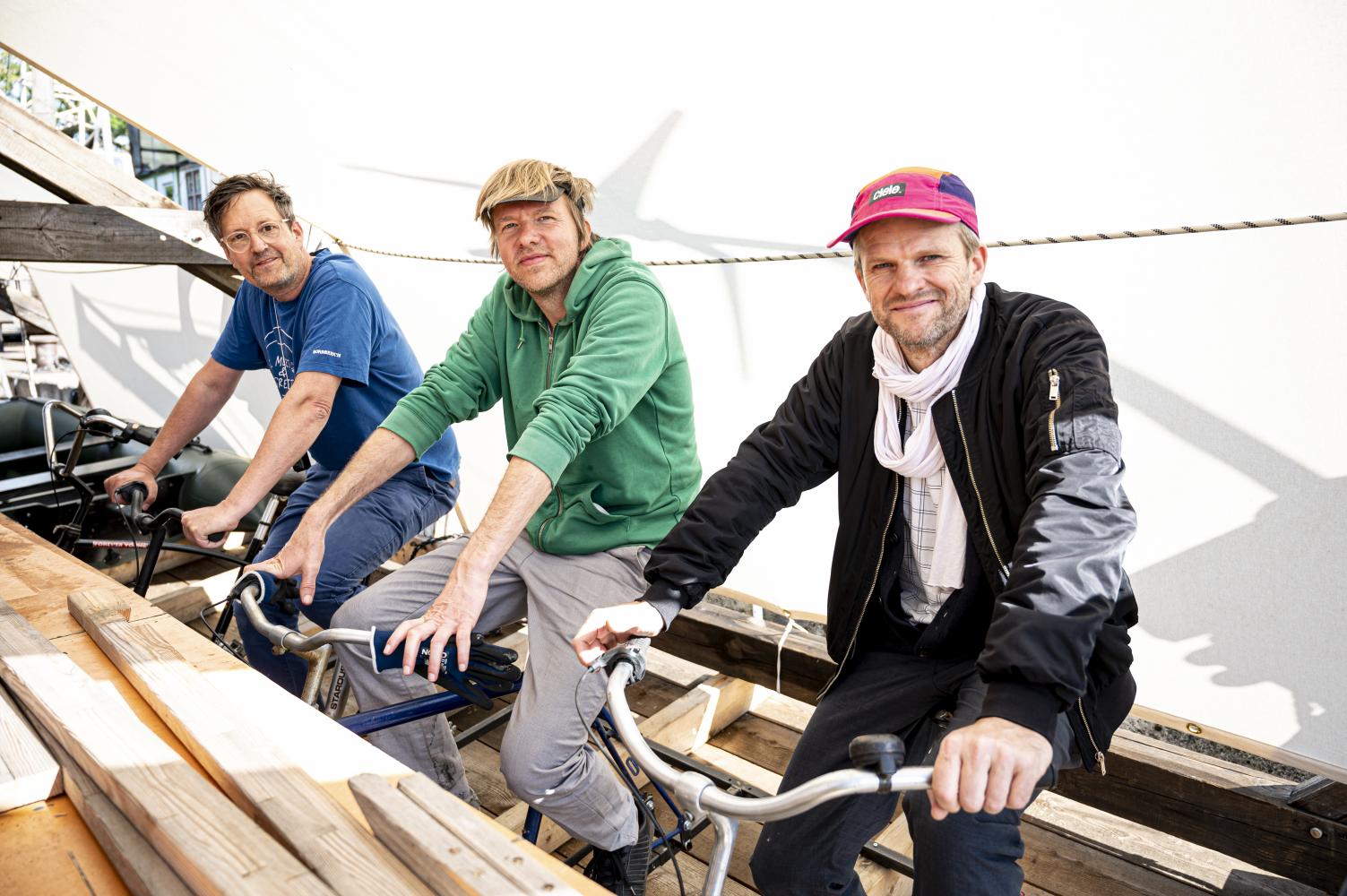 Von links: das Künstler-Trio Philip Horst, Harry Sachs und Matthias Einhoff treten auf dem Schiff "Citizenship" in die Pedale der angebrachten Fahrräder. Für das Projekt wurde die Dachkonstruktion des Berliner Zentrums für Kunst und Urbanistik als Floß umgestaltet